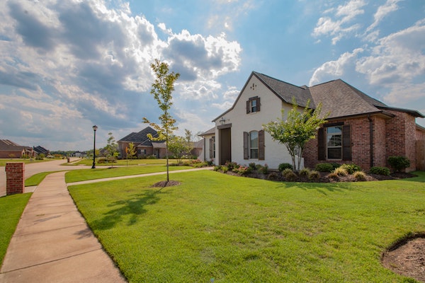 white and brown house with a green front lawn